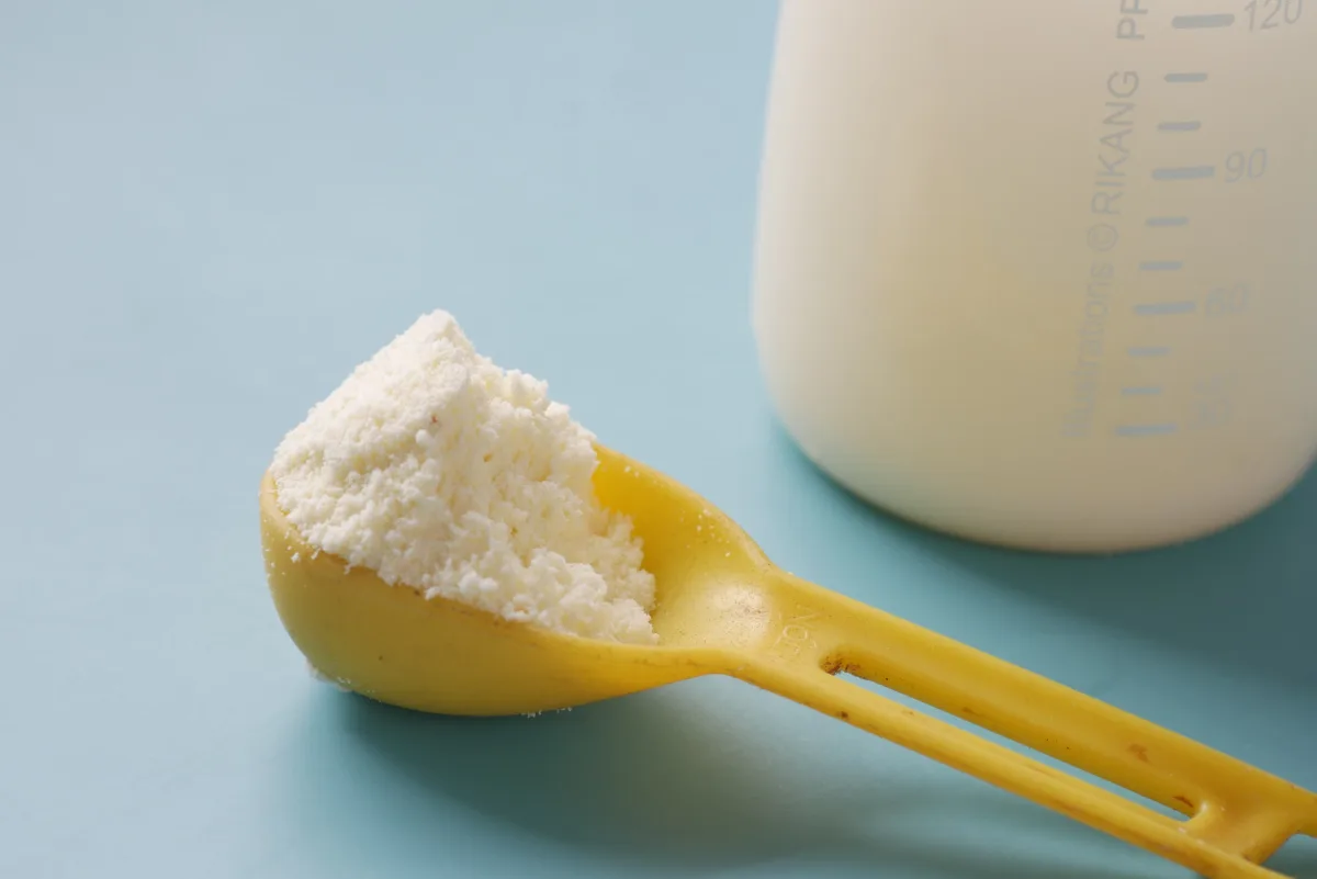Close-up of powdered baby formula in a yellow scoop with a measuring bottle