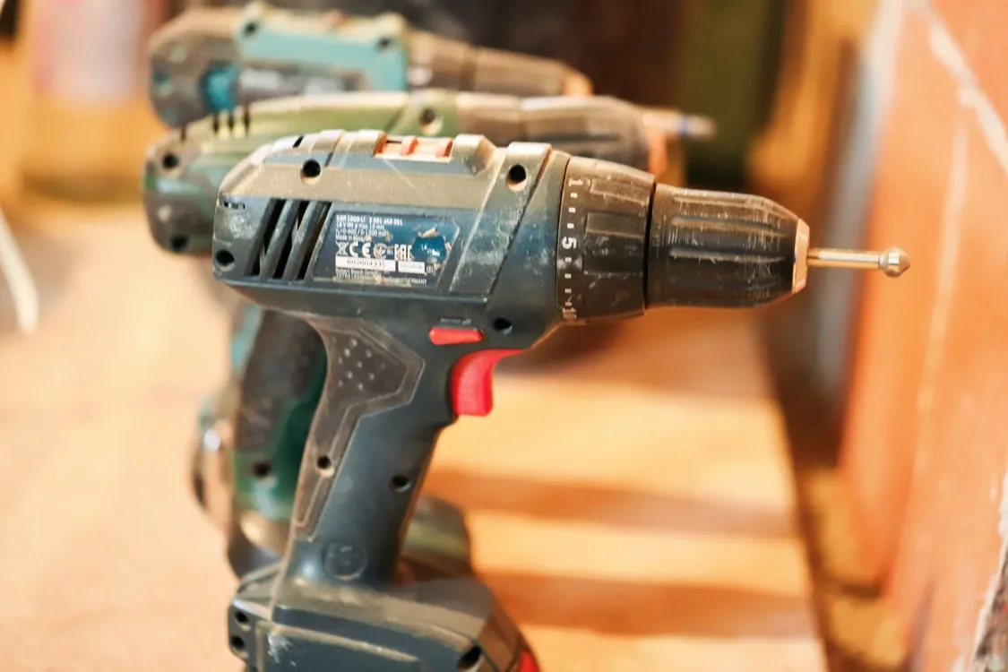 A row of cordless power drills on a wooden workbench ready for use