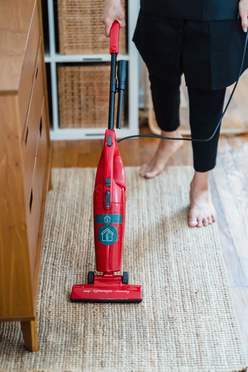Woman using a cordless stick vacuum cleaner on hardwood floors in a bright modern living room