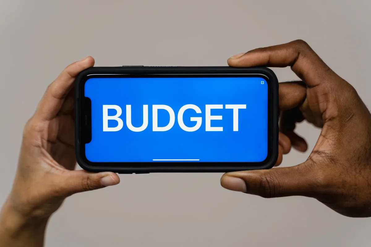 Hands holding smartphone displaying "budget" text — budgeting app pricing breakdown