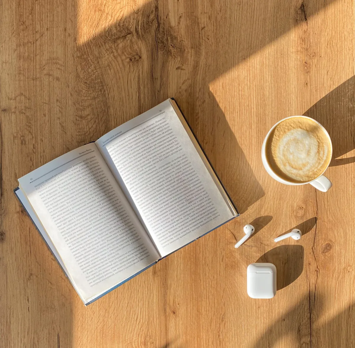 Open book, coffee cup, and wireless earphones on a wooden table for a cozy reading setup