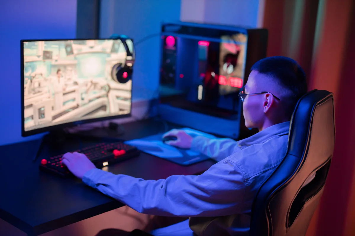 Young man gaming intently at a modern computer setup with multiple peripherals