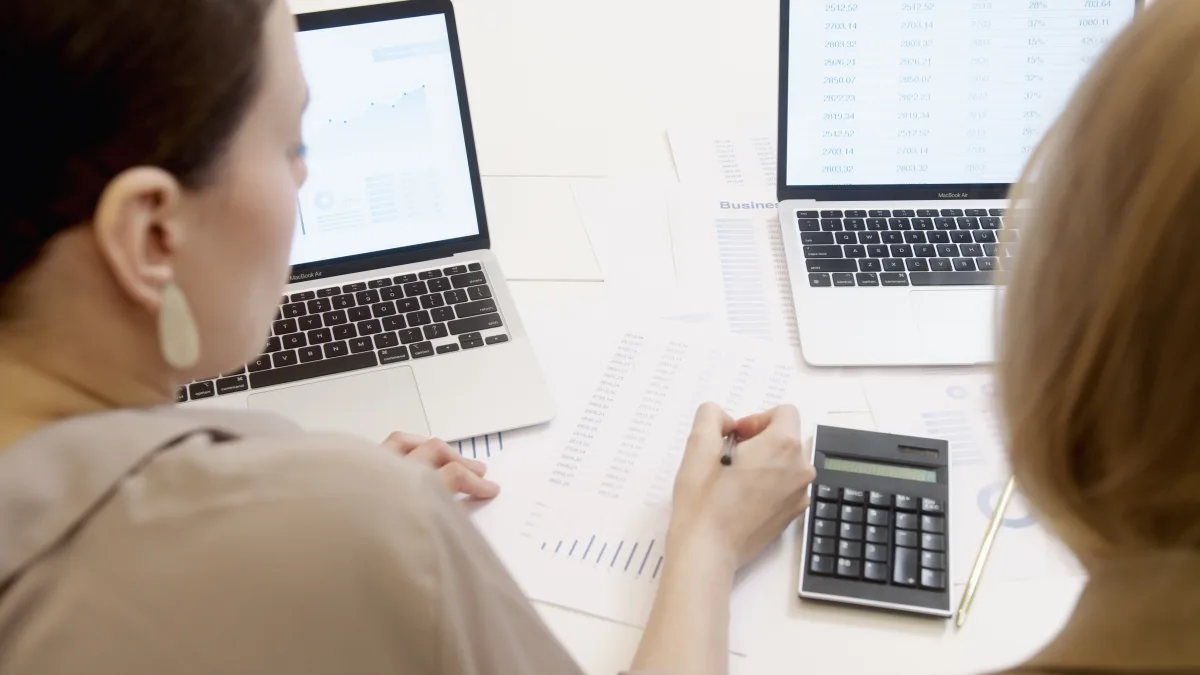 Two people reviewing investment data on laptops with charts and graphs