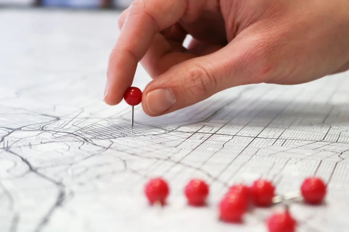 Hand placing a red pin on a geographic map indicating a location