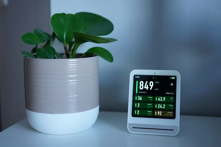 Air quality monitor next to a potted plant showing PM2.5 and CO2 levels