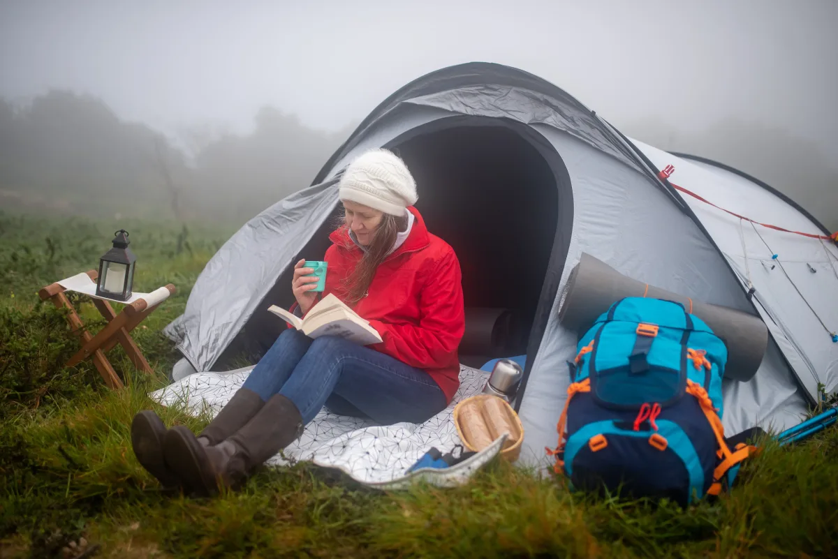 Camper in sleeping bag reading inside a tent on a misty morning