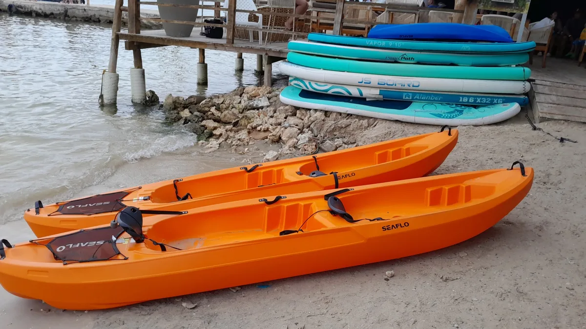 Bright orange kayaks and paddleboards resting on a sandy beach near calm water