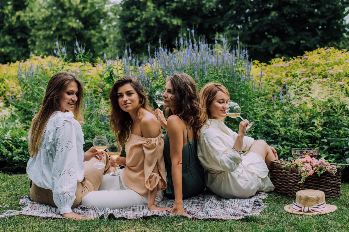 Four women enjoying outdoor picnic with wine in garden setting