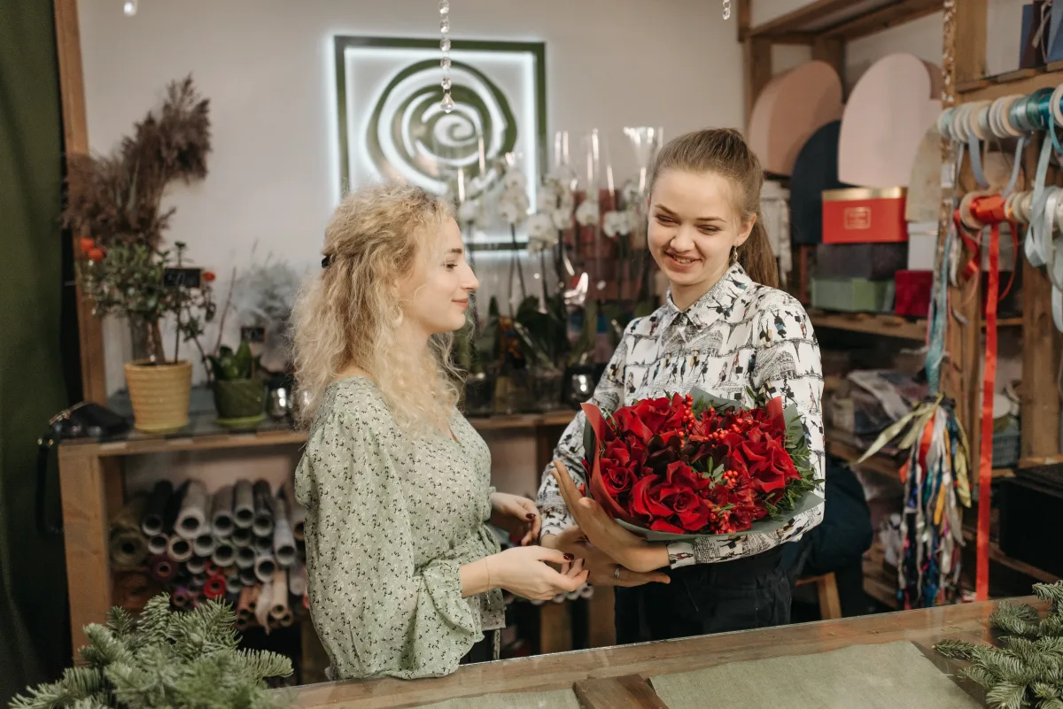 Two women exchanging a vibrant red bouquet at a cozy flower shop counter