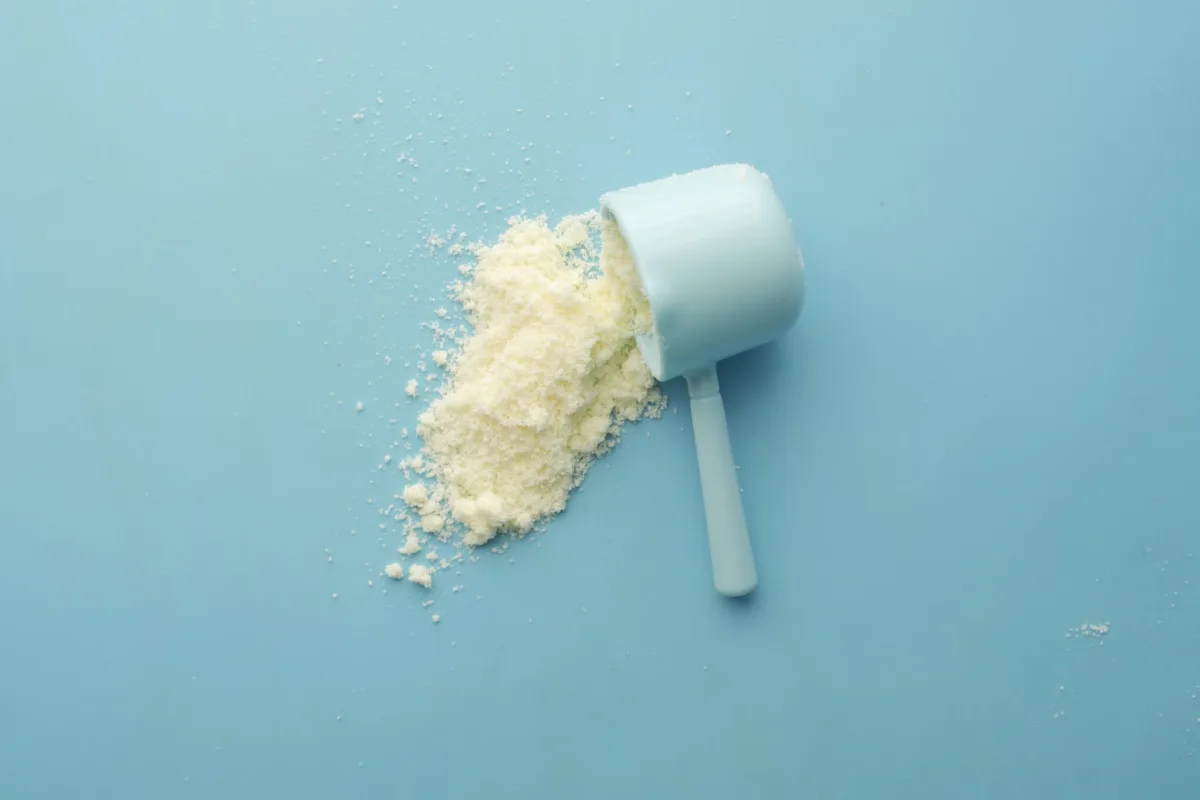 White protein powder spilled from scoop on blue background