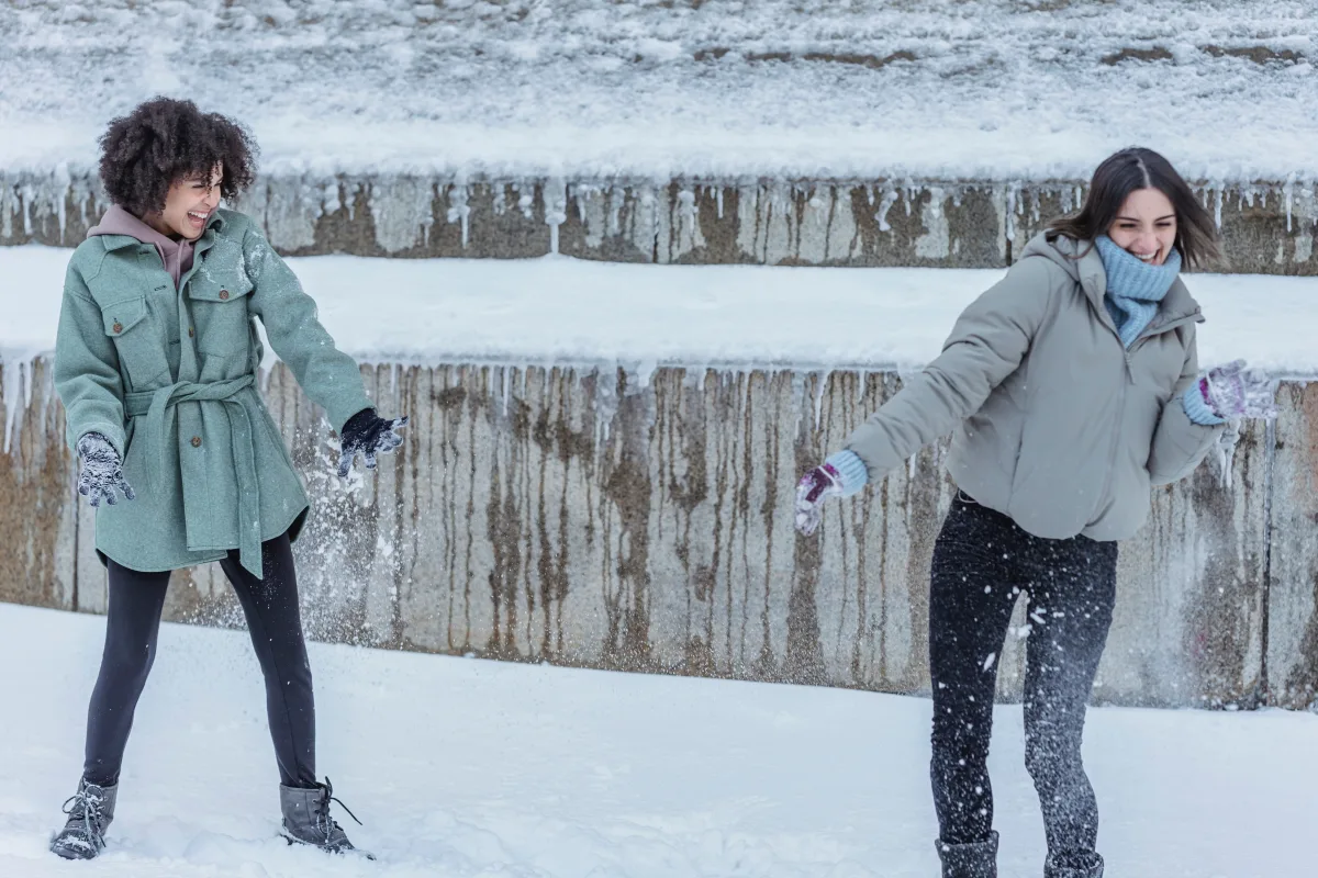 Women laughing in mid-range winter coats in snowy park