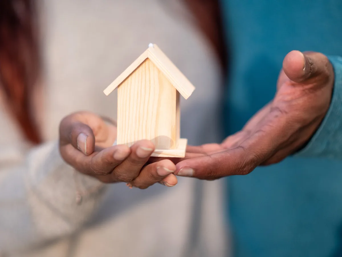Hands holding a small wooden house model representing homeownership