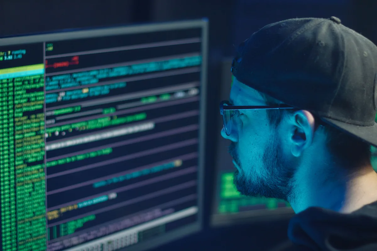 Cybersecurity expert inspecting lines of code on multiple monitors