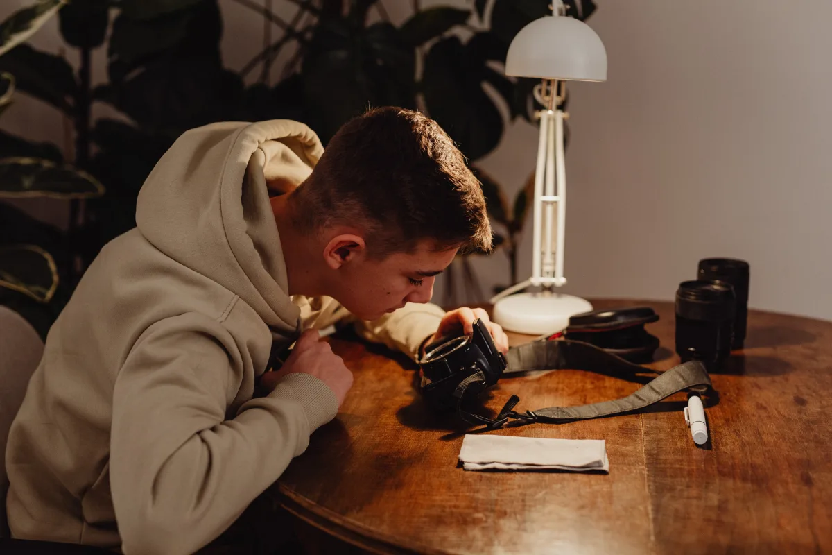 Young photographer examining mirrorless camera at desk with accessories