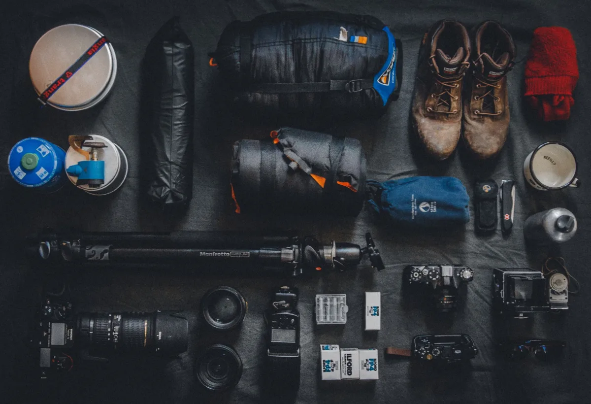 Flat lay of outdoor camping gear including water bottle, compass and equipment
