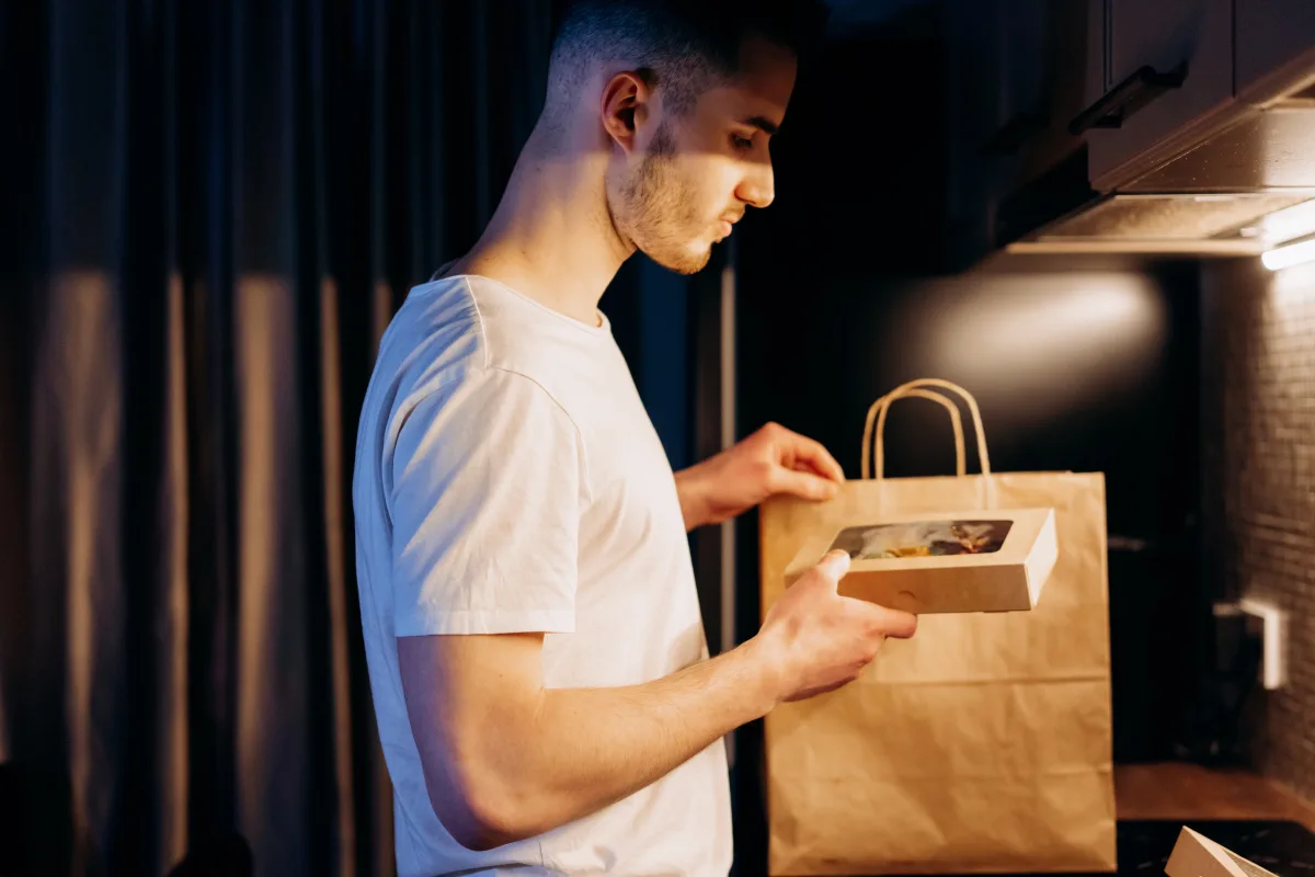 Man unpacking a meal kit from a paper bag in a warmly lit kitchen
