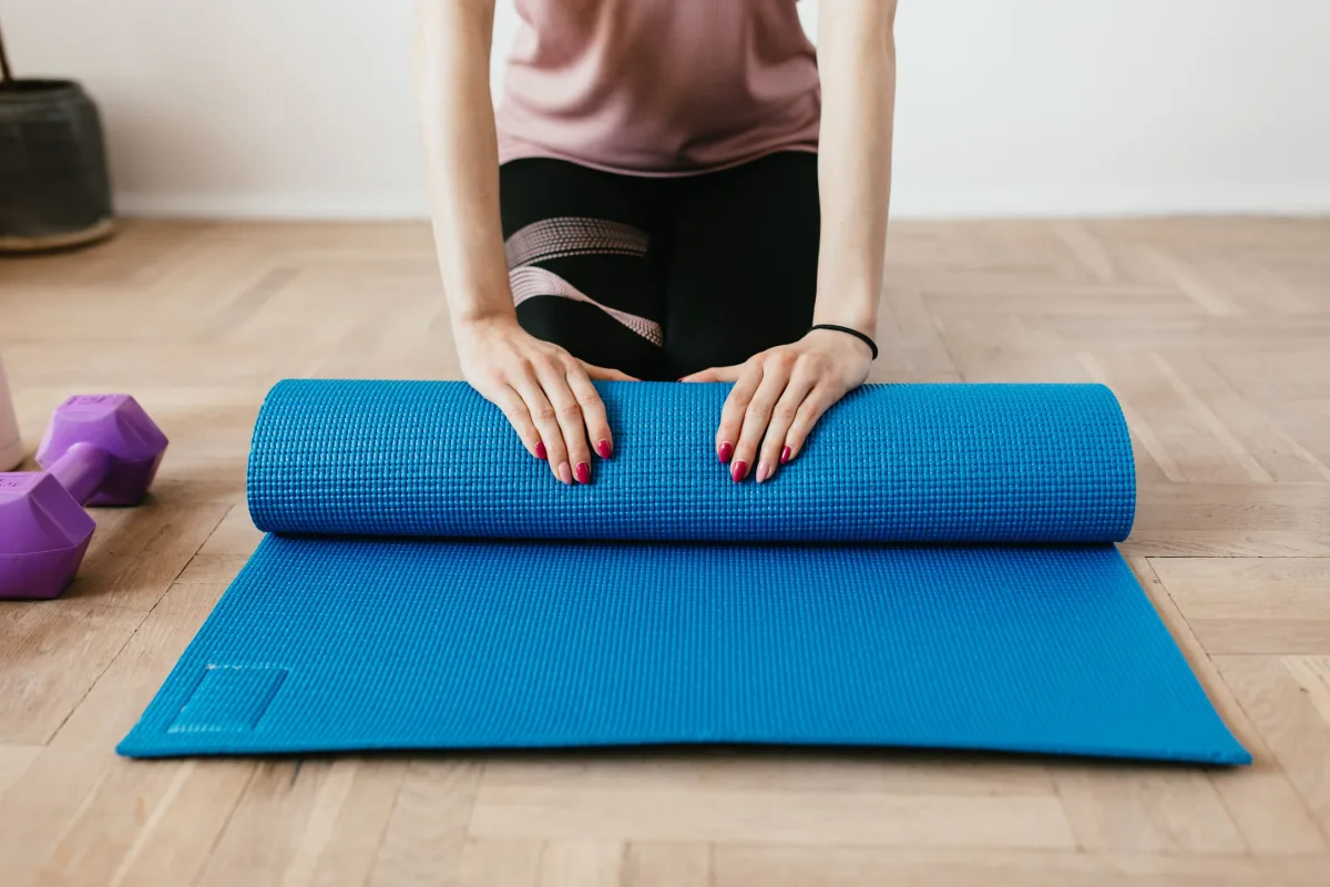 Woman unrolling a thick Pilates mat on hardwood floor at home