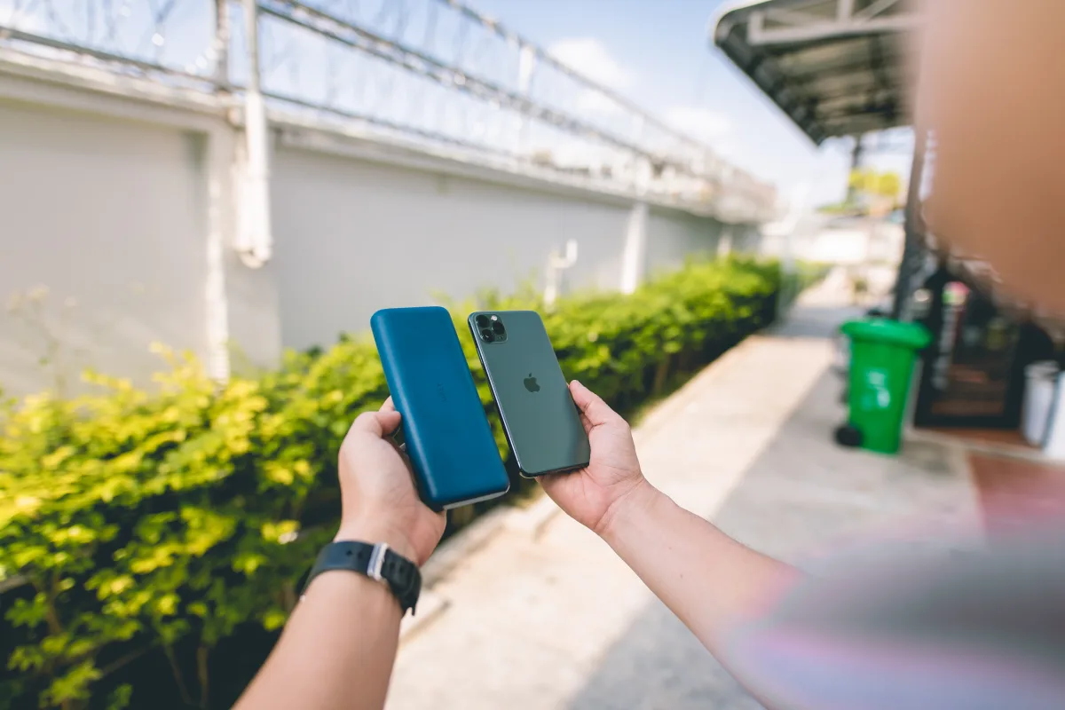 Person holding smartphone connected to power bank in outdoor setting
