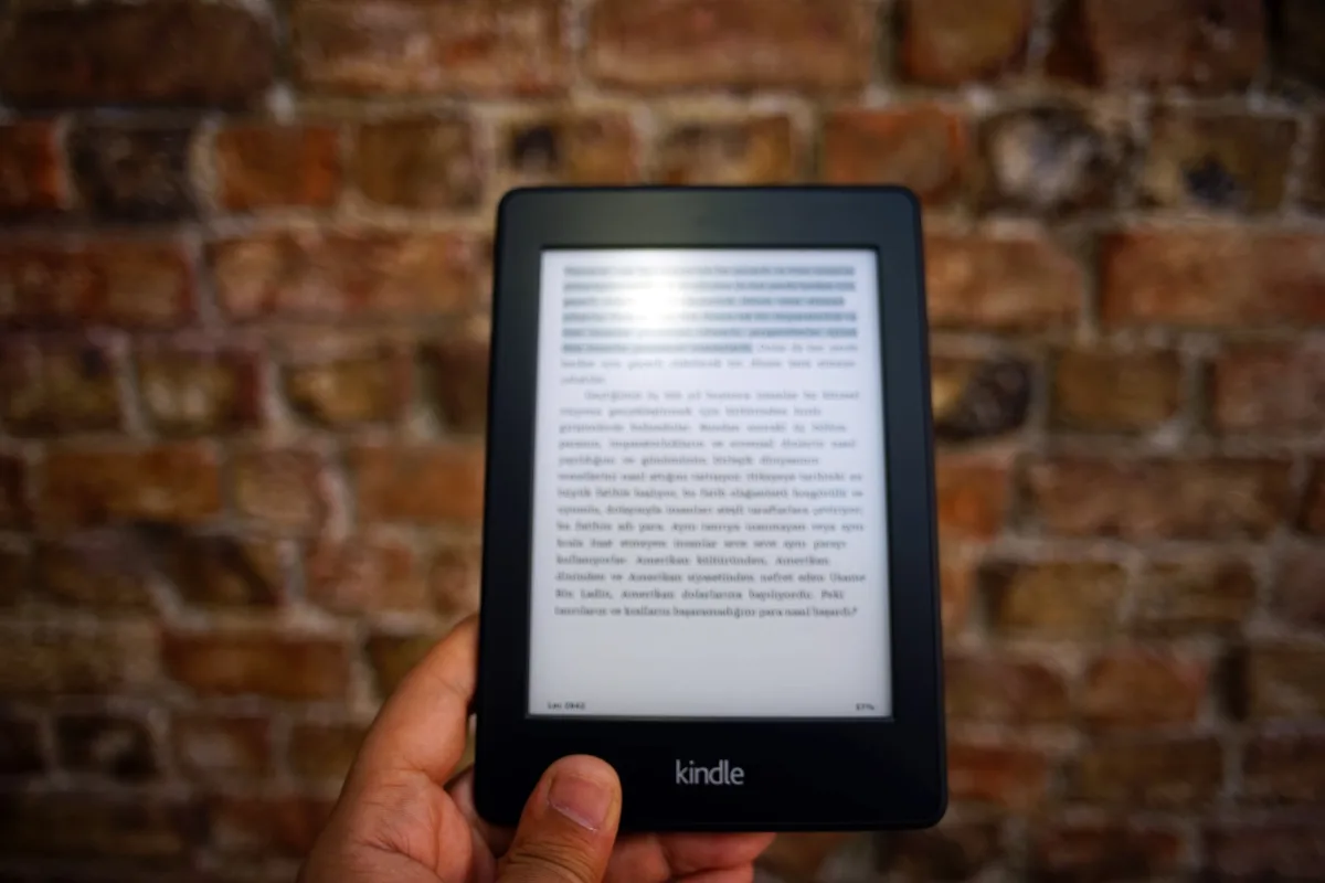 Close-up of a Kindle e-reader against a textured brick wall