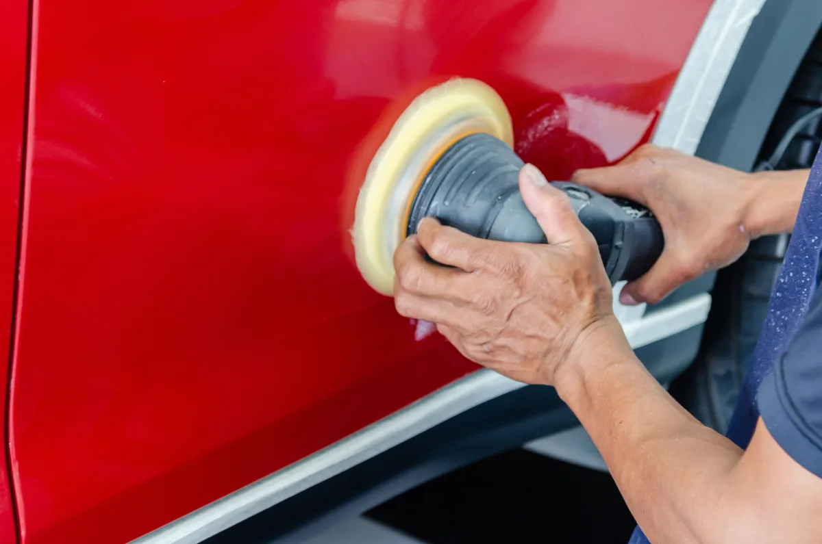 Worker buffing red car paint (side panel, close-up)