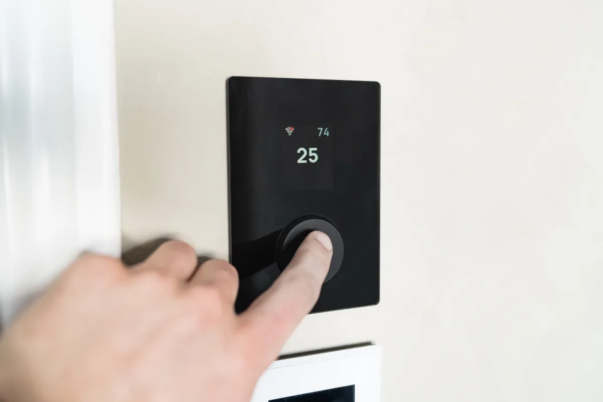 Person interacting with a sleek wall-mounted smart thermostat