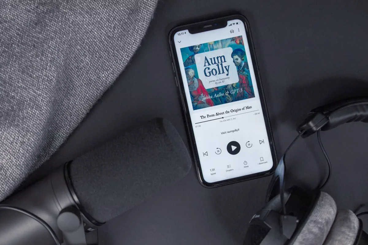 Flatlay of audiobook setup with headphones, smartphone and microphone on dark background