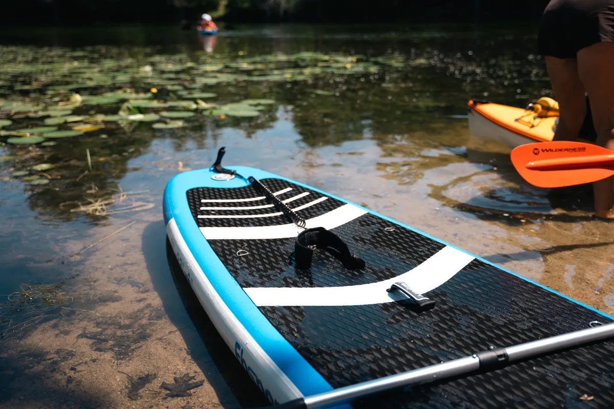Paddleboard and kayak resting beside a tranquil lake with water lilies