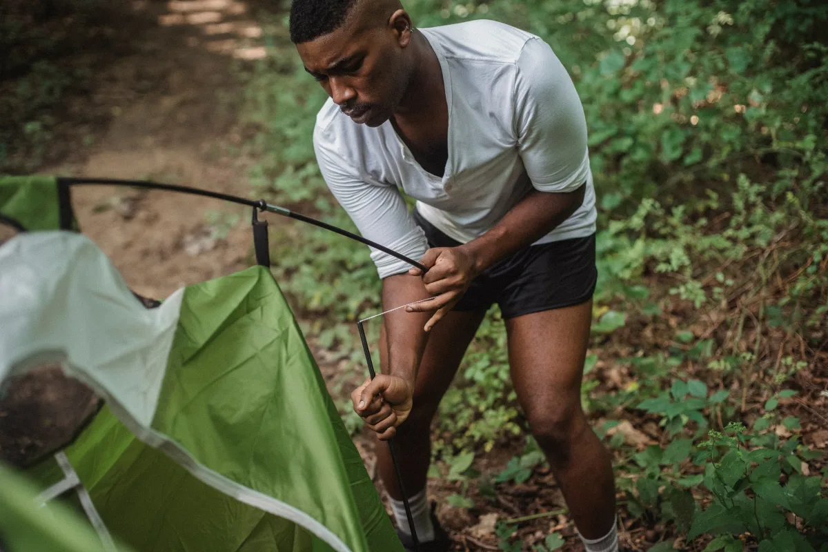 Young hiker setting up a green tent alone in a forest