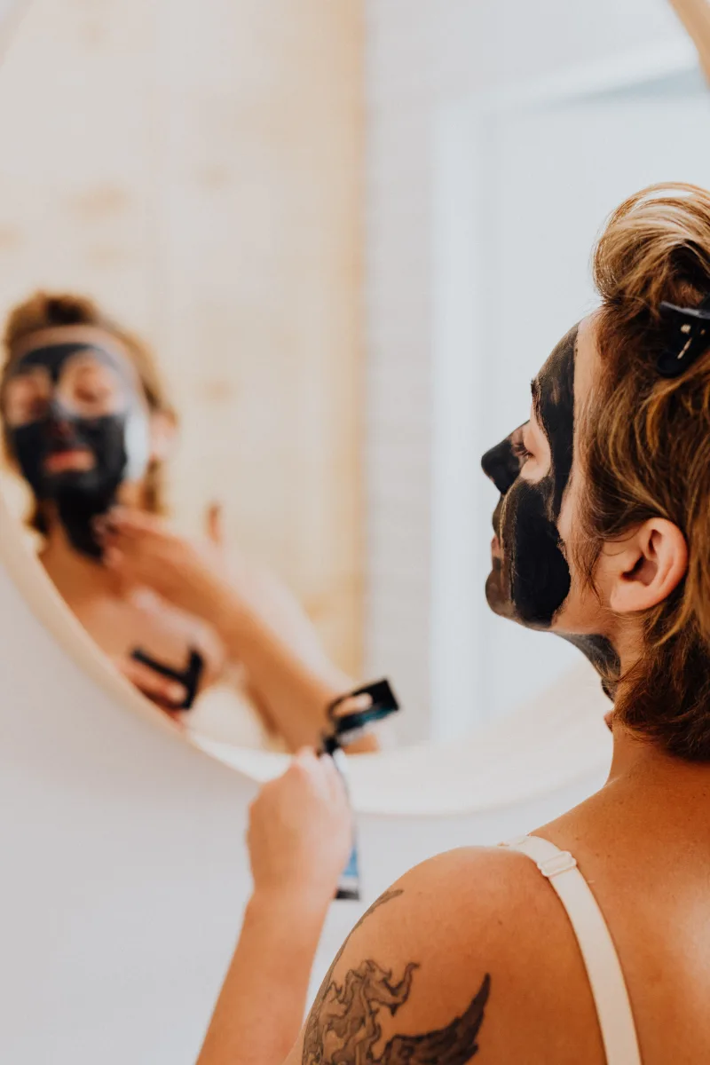 Woman applying nighttime skincare treatment in front of bathroom mirror