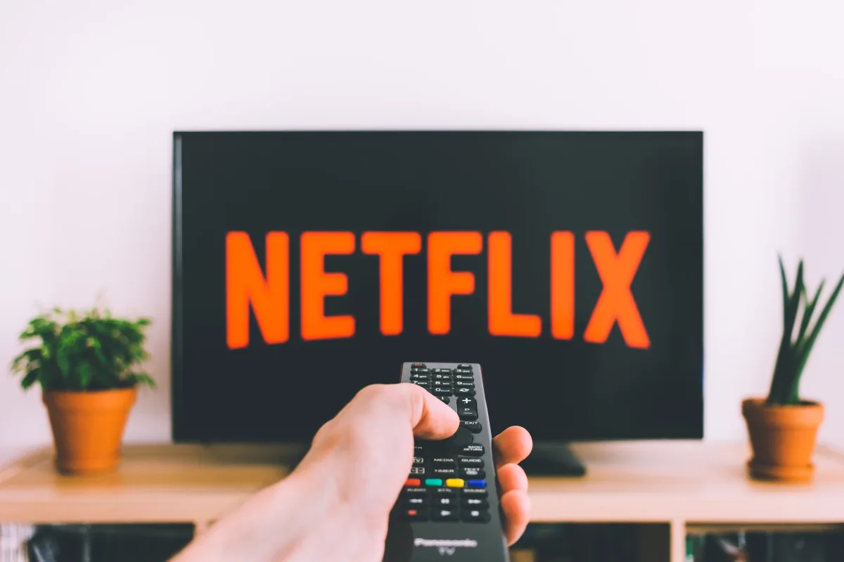 Hand holding TV remote pointed at a screen showing Netflix