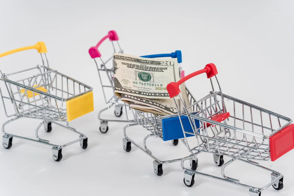Miniature shopping carts with dollar bills representing retail savings