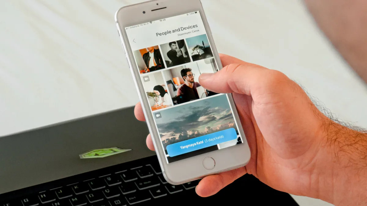 Close-up of hand scrolling phone with laptop in background, online research
