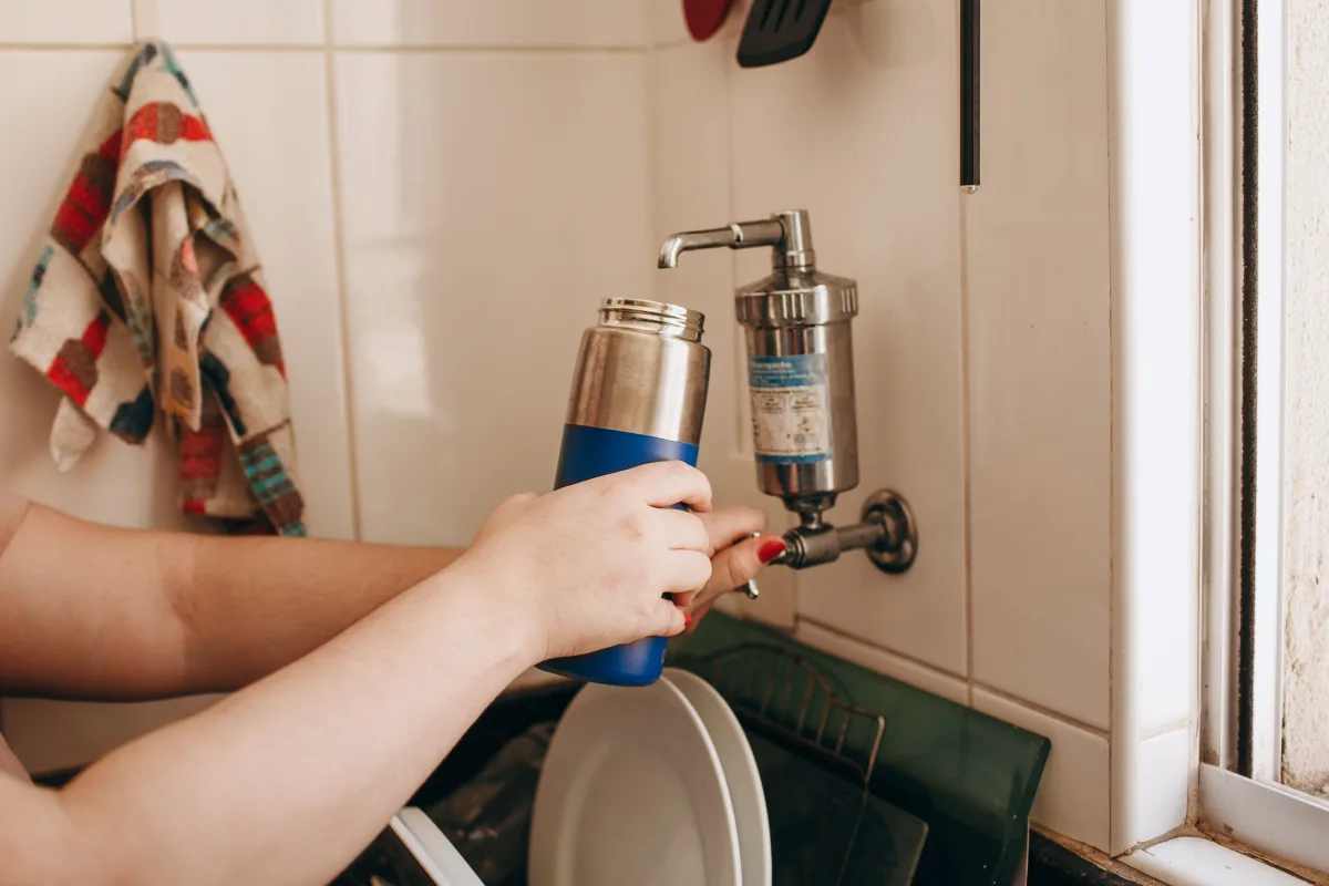 Close-up of hands filling a water bottle at an indoor kitchen faucet